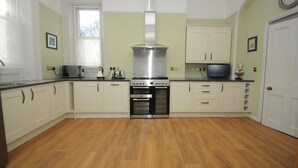 Una cocina con armarios blancos, una campana extractora de acero inoxidable, un microondas, un tostador y un televisor.