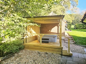 A wooden outdoor structure with a roof, a small enclosed area, and a gravel pathway leading to it.