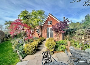 A brick house with a front garden, a paved pathway leading to the entrance, and outdoor furniture.
