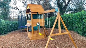 A wooden play structure with a swing set and a slide, surrounded by mulch and greenery. - Criddlestyle Cottage Fordingbridge (Fordingbridge)