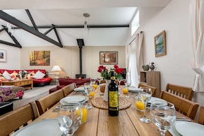 Un coin repas avec une table en bois dressée pour le dîner, une bouteille de vin et une cheminée en arrière-plan.