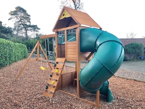 A wooden play structure with a slide and swings.