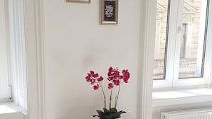 Une console blanche, ornée d’une orchidée en pot, est placée devant une fenêtre. Trois tableaux encadrés sont accrochés au mur, au-dessus de la console.