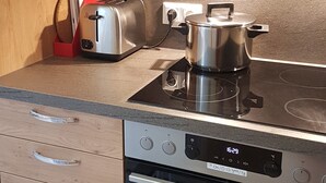 Une cuisine avec des meubles de rangement en bois, un grille-pain, une casserole sur une plaque de cuisson à induction et un four.