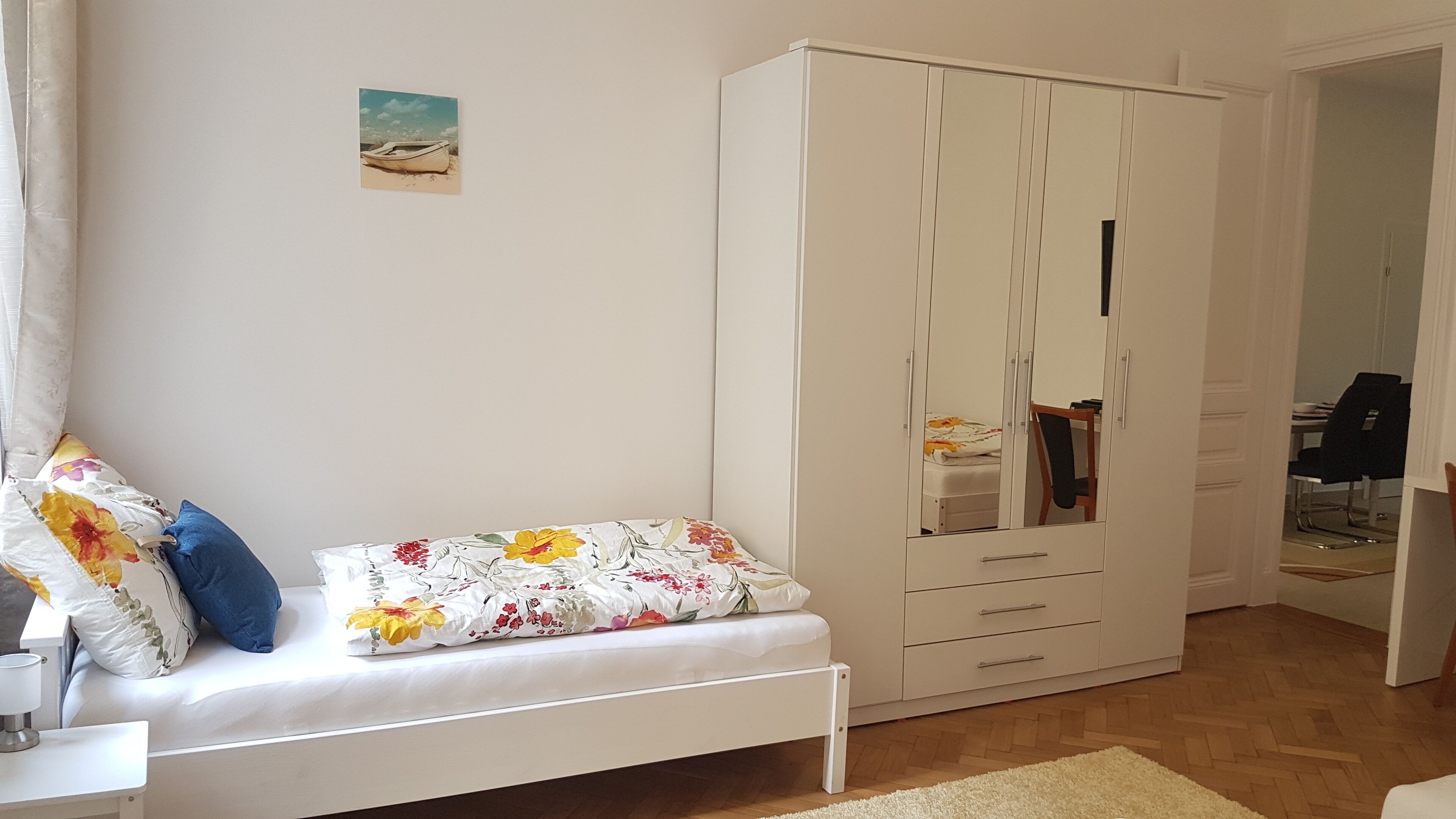 A bedroom with a bed, a white wardrobe, and a small table with a lamp.