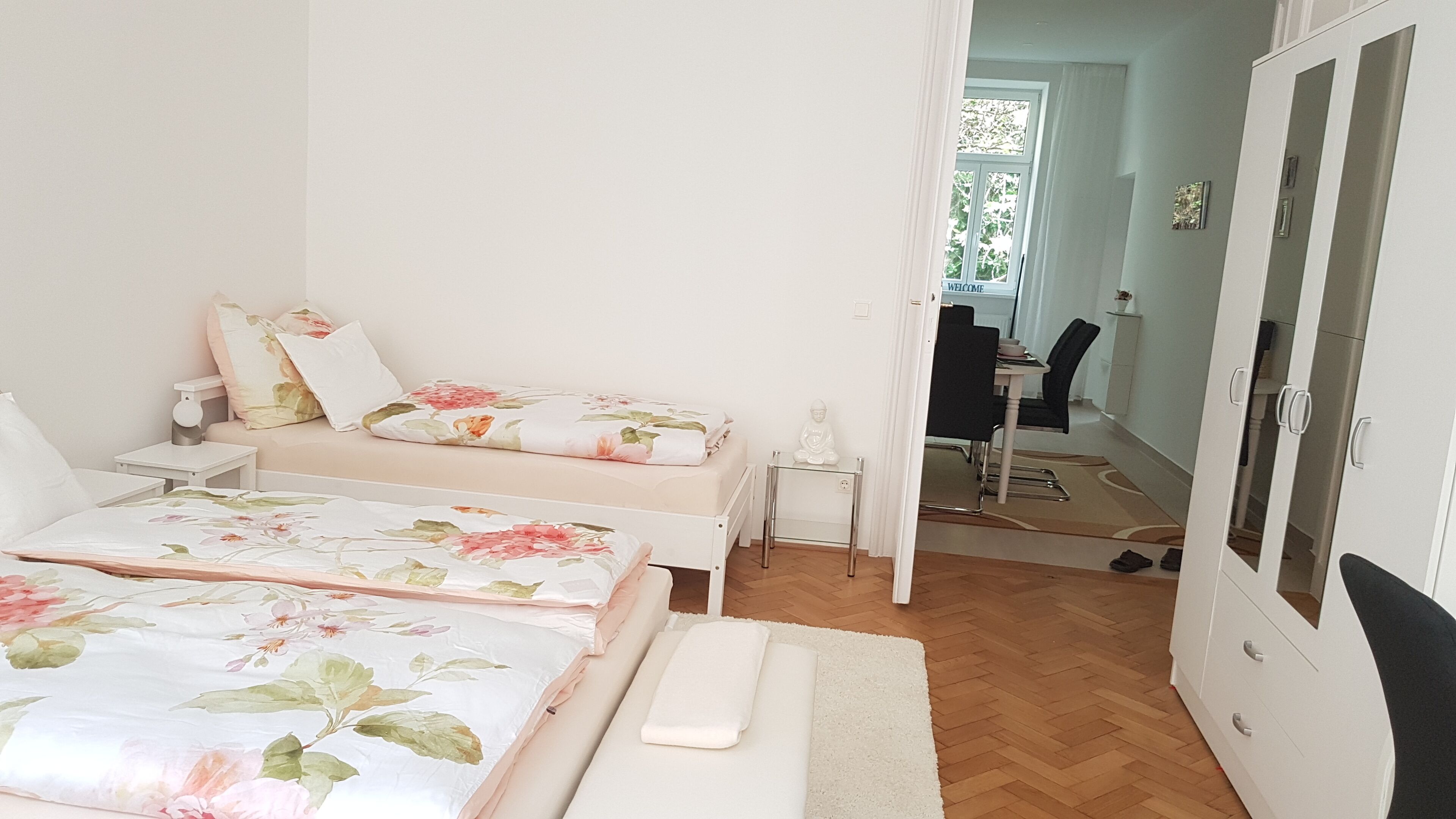 A bedroom with two beds, a desk, and a wardrobe.
