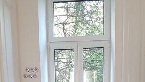 Une pièce avec un radiateur blanc, un banc et une fenêtre sur laquelle est affiché un panneau indiquant « BIENVENUE ».
