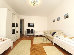 Um quarto moderno e bem iluminado com sofá, uma mesinha, televisão e guarda-roupa.