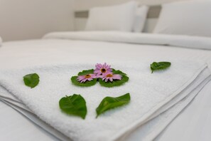 A neatly folded white towel with green leaves and pink flowers on a bed. - Mitos Apartments (İçmeler)