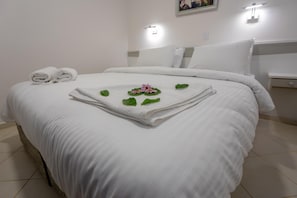 A neatly made bed with white linens, a floral arrangement on the bed, and a wall-mounted light fixture. - Mitos Apartments (İçmeler)