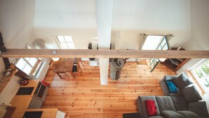 Amplo quarto estilo loft com teto alto, piso de madeira e grandes janelas que permitem entrada de luz natural.