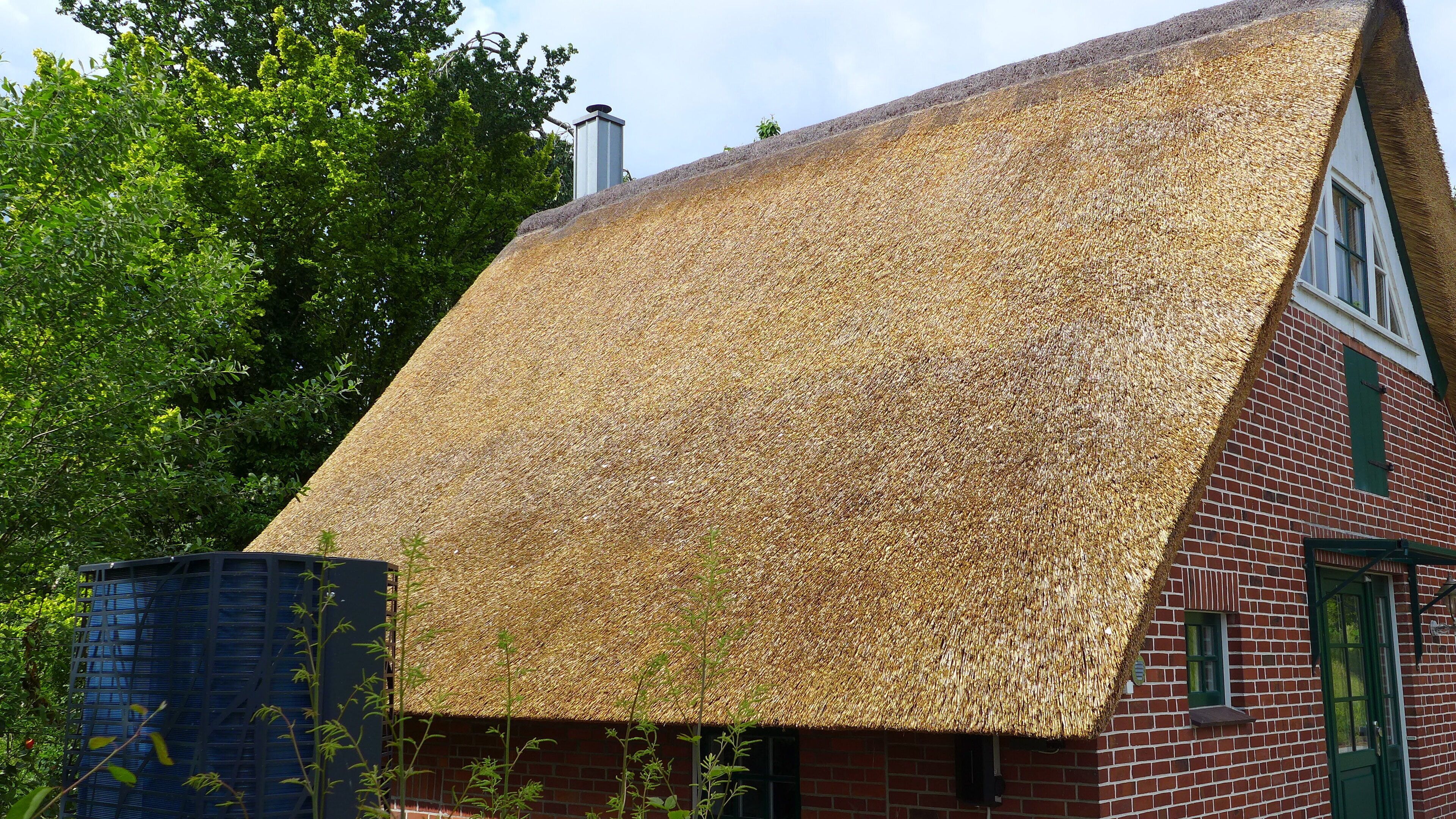 A traditional thatched-roof house with a brick exterior, a chimney, and a window with a green shutter.