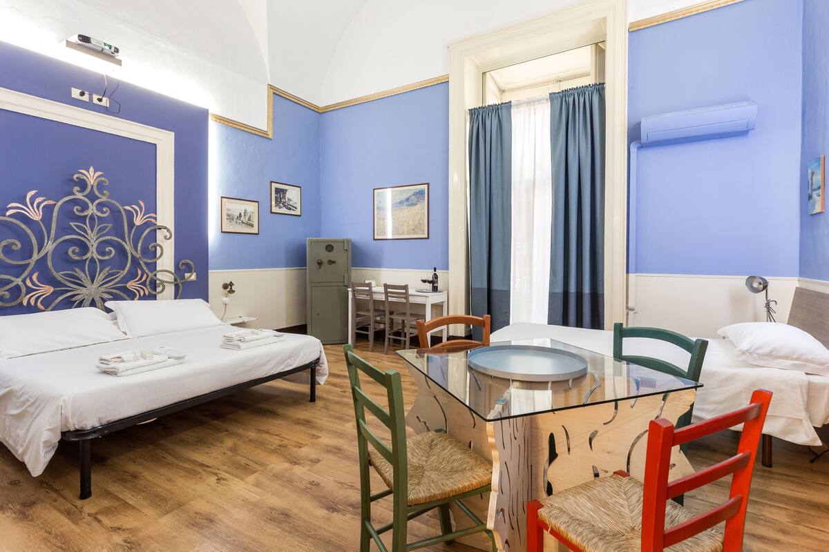 A hotel room with two beds, a glass dining table, and a small kitchenette.
