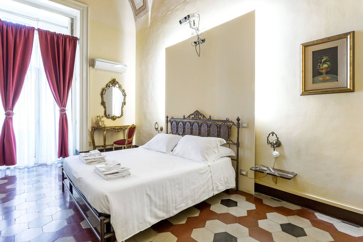 A hotel room with a large bed, a mirror, a framed picture on the wall, and a window with curtains.