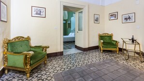 Una habitación con dos sillones tapizados en verde, una mesita con superficie de vidrio y una cama al fondo.