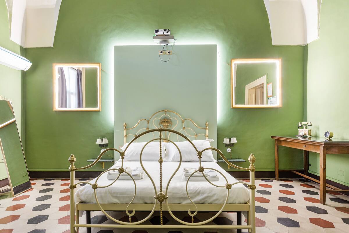 A room with a bed, a mirror, a table, and a ceiling light.