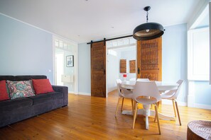 A living room with a sofa, dining table, chairs, and a hanging light fixture. - Sé Apartment: A charming nest by the Cathedral (Lisboa)