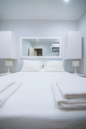 Une chambre d’hôtel moderne, dotée d’un grand lit, de deux tables de chevet, d’un miroir et d’un climatiseur fixé au mur.