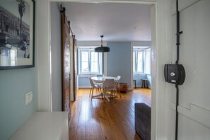 Un couloir mène à une salle à manger où se trouvent une table ronde et des chaises, un luminaire suspendu et une porte équipée d’un dispositif de sécurité.
