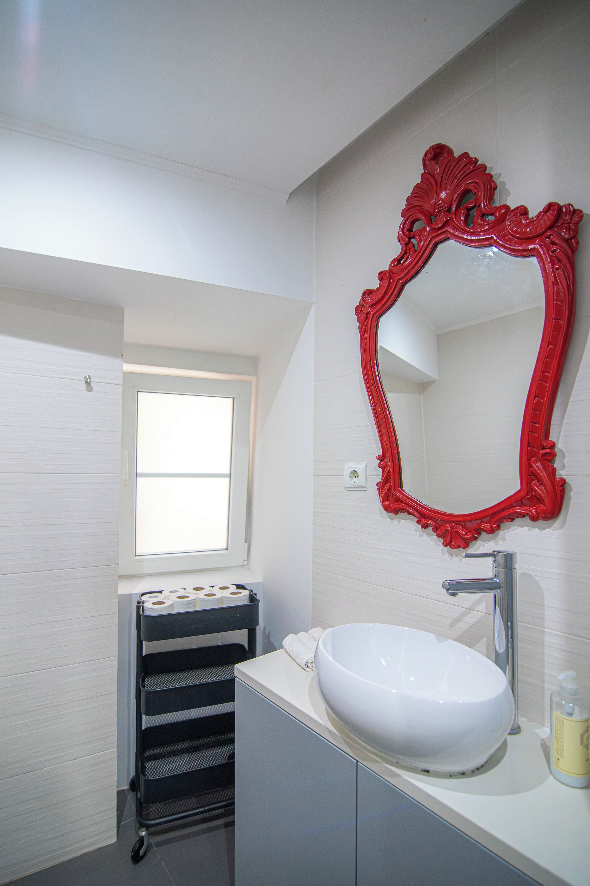 A bathroom with a white sink, a red ornate mirror, a window, and a towel rack with towels.