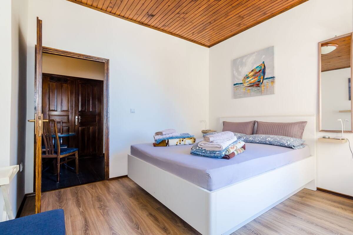 A bedroom with a bed, a wooden ceiling, a painting, and a mirror.