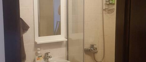 Un baño con ducha de vidrio, un lavamanos con espejo y una toalla colgada en la pared.