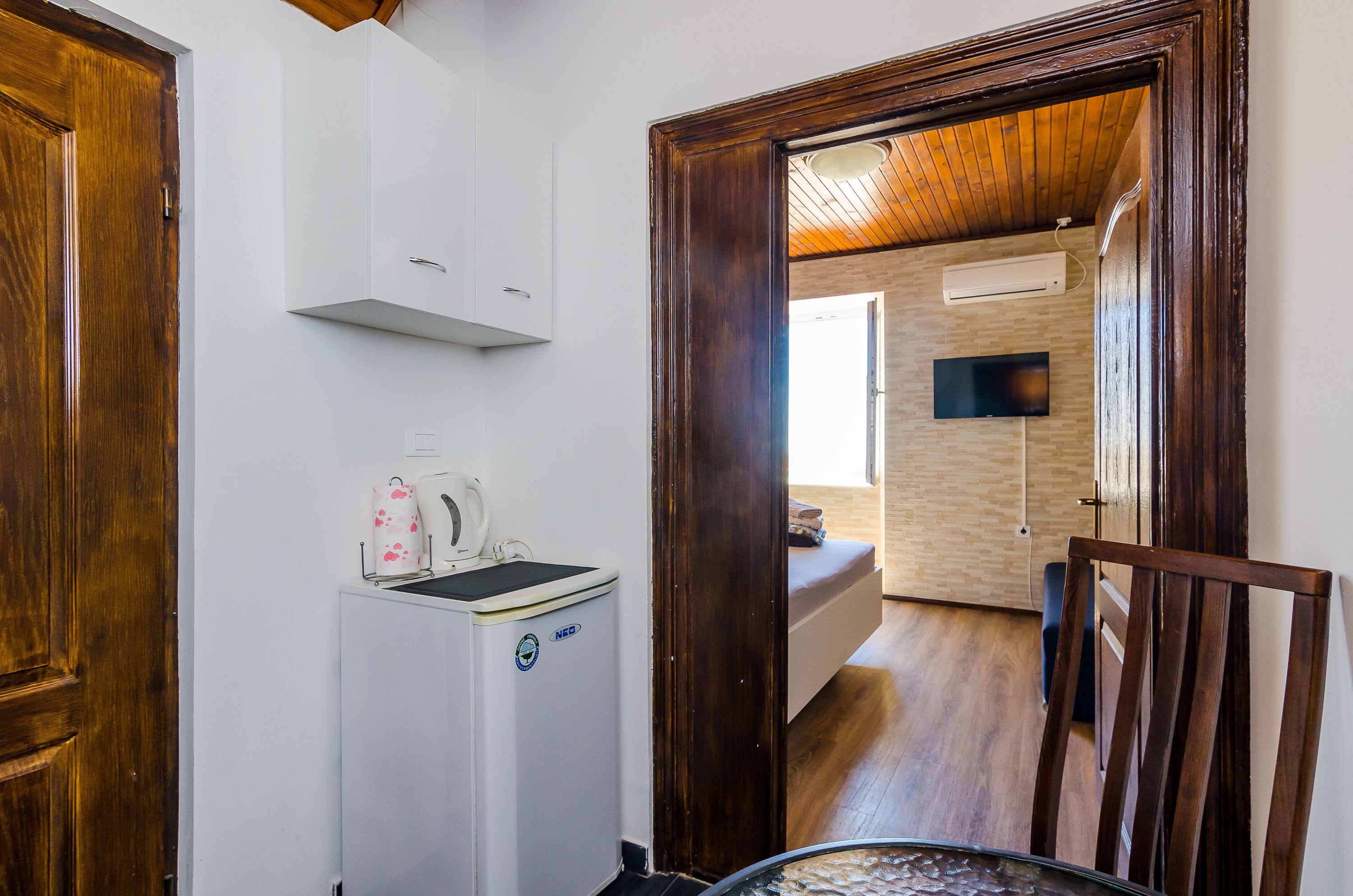 A compact kitchen with a white refrigerator, a wooden cabinet, and a wooden chair.