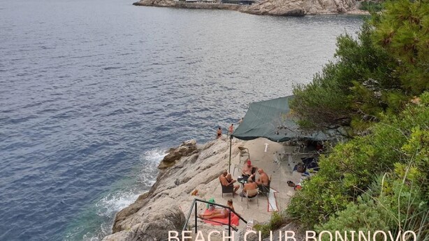 A coastal view with a rocky beach area and a building complex in the background. - Rooms City Central Old Town (Dubrovnik)