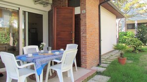 An outdoor patio with a table set for two, white plastic chairs, and a coffee maker.
