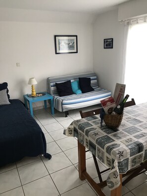 A bedroom with a bed, a bedside table with a lamp, a sofa, and a window with curtains.