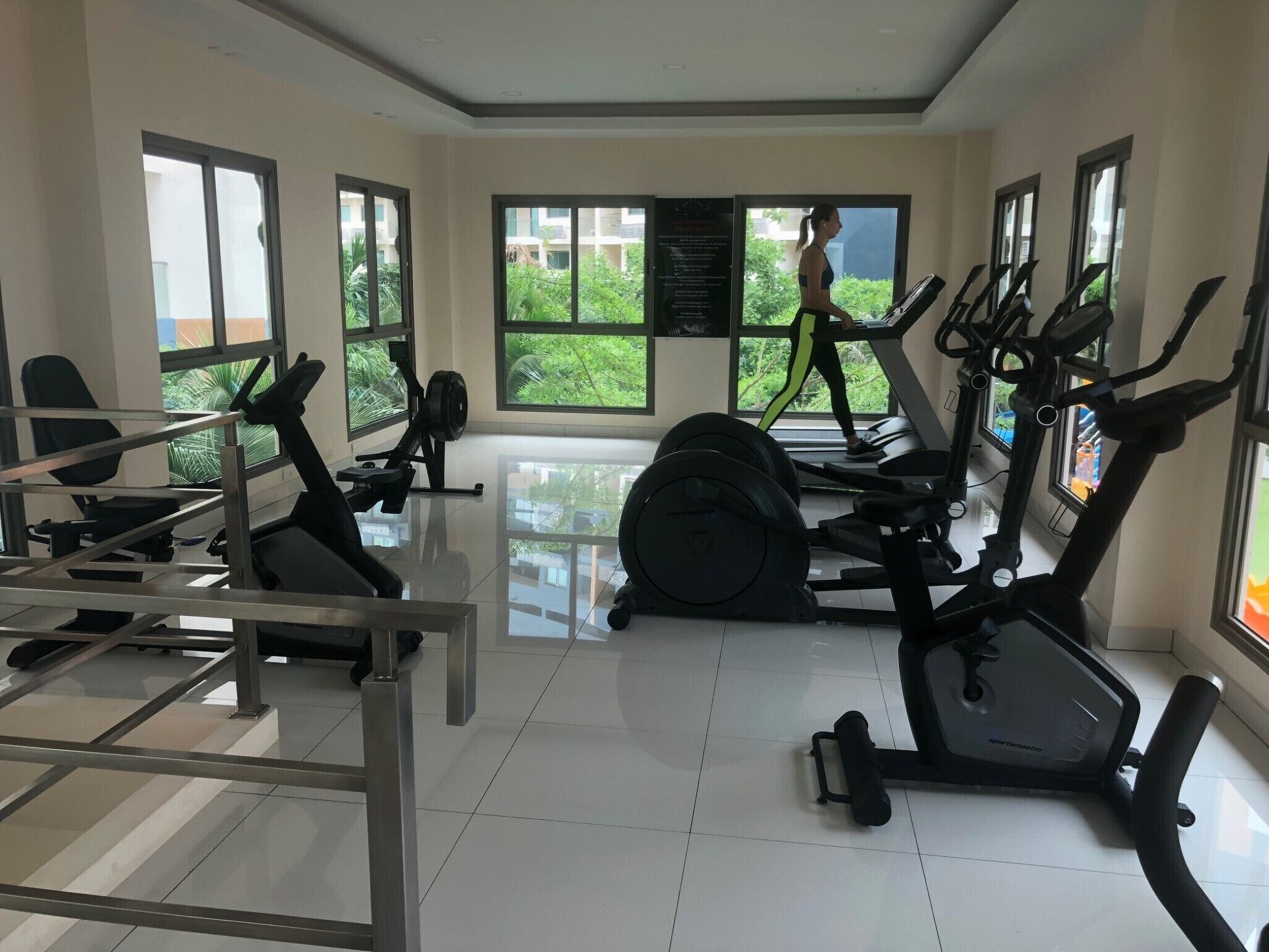 A gym with exercise equipment, large windows, and a view of greenery.