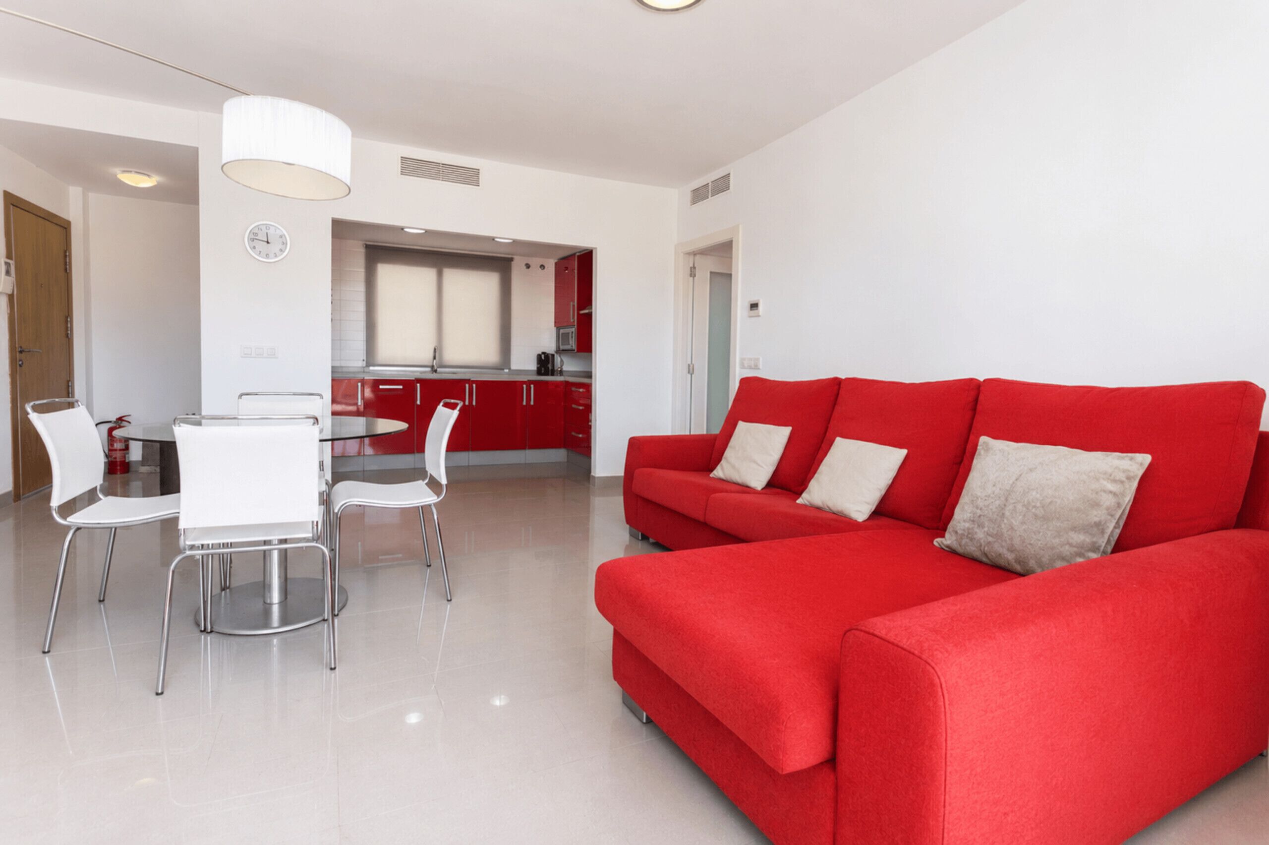 Een moderne woonkamer met een rode bank, een eethoek met witte stoelen, en een keuken op de achtergrond.
