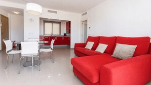 A modern living room with a red sofa, a dining area with white chairs, and a kitchen in the background. - Big Terrace Apartment Cullera (Cullera)