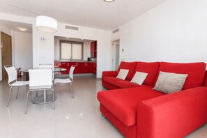 Una sala de estar moderna con un sofá rojo, un comedor con sillas blancas y una cocina al fondo.