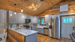 Une cuisine dotée d’un plafond en bois, de plans de travail en granit, d’appareils électroménagers en acier inoxydable et d’un grand îlot central.