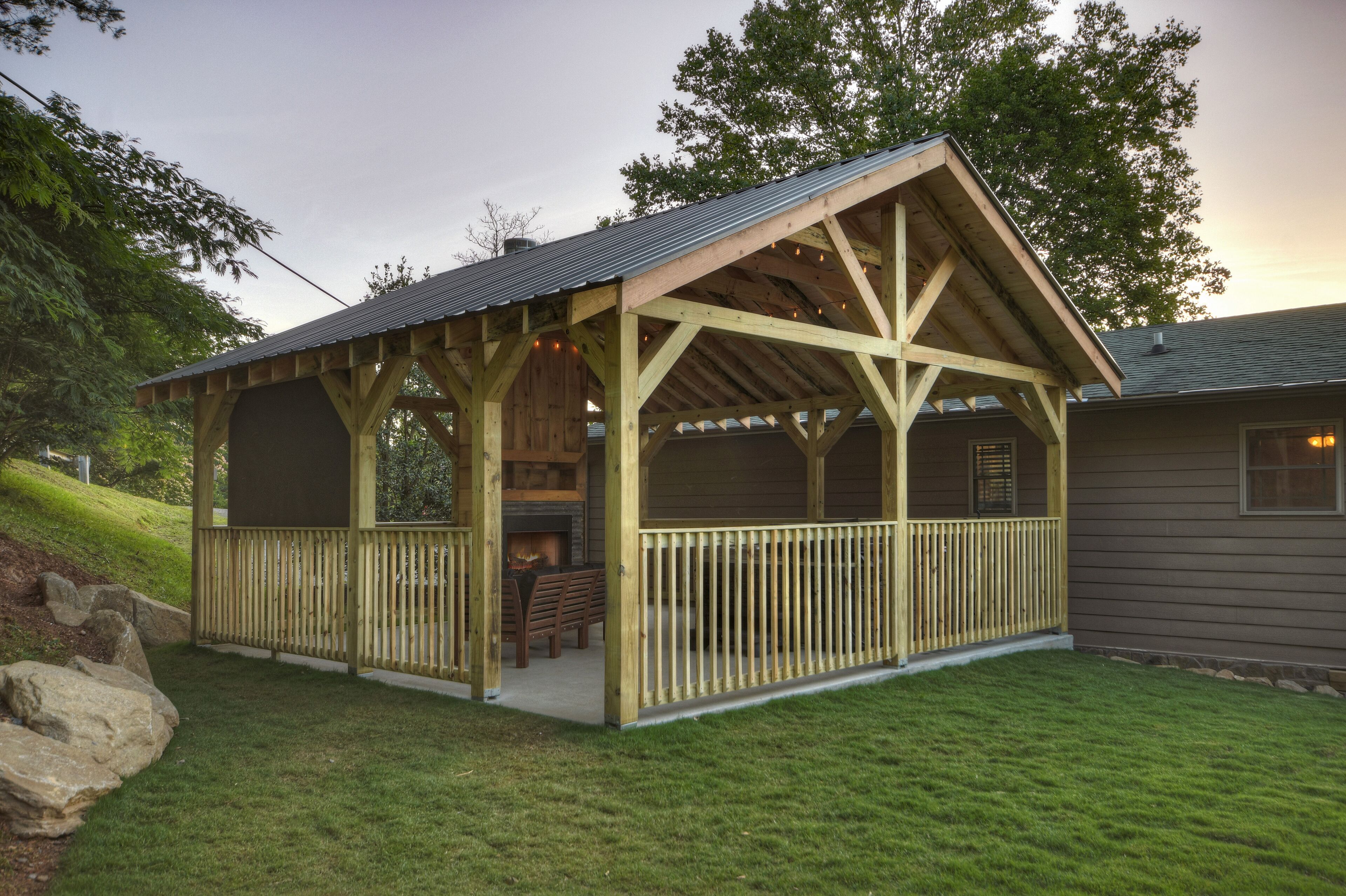 A wooden gazebo with a metal roof, surrounded by a wooden deck and a stone wall.