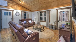 Un salon chaleureux avec un canapé en cuir marron, une table basse en bois et une cheminée. Des rideaux sont accrochés aux fenêtres et une horloge est fixée au mur.