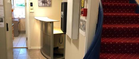 A hotel corridor with a red carpeted staircase, a kitchenette area, and a fire alarm on the wall.