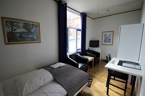A room with a bed, a desk, a chair, a television, and a window with curtains. - Ami hotel (Tromsø)