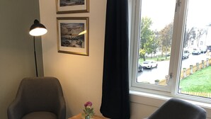 Et værelse med to grå lænestole, et træbord med en vase og billeder i rammer på væggen.