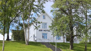 En hvid bygning med skilt, der viser "AMI HOTEL" øverst. Der er trapper, der fører op til indgangen.