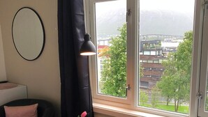 Et moderne værelse med stort vindue, et rundt spejl, en sort læderstol, et træbord med lyserød vase og en lyserød pude.
