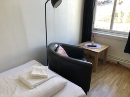 Una habitación de hotel con una cama, un sillón de cuero negro, una pequeña mesa de madera con un florero y una ventana que da a vista de motocicletas estacionadas afuera.