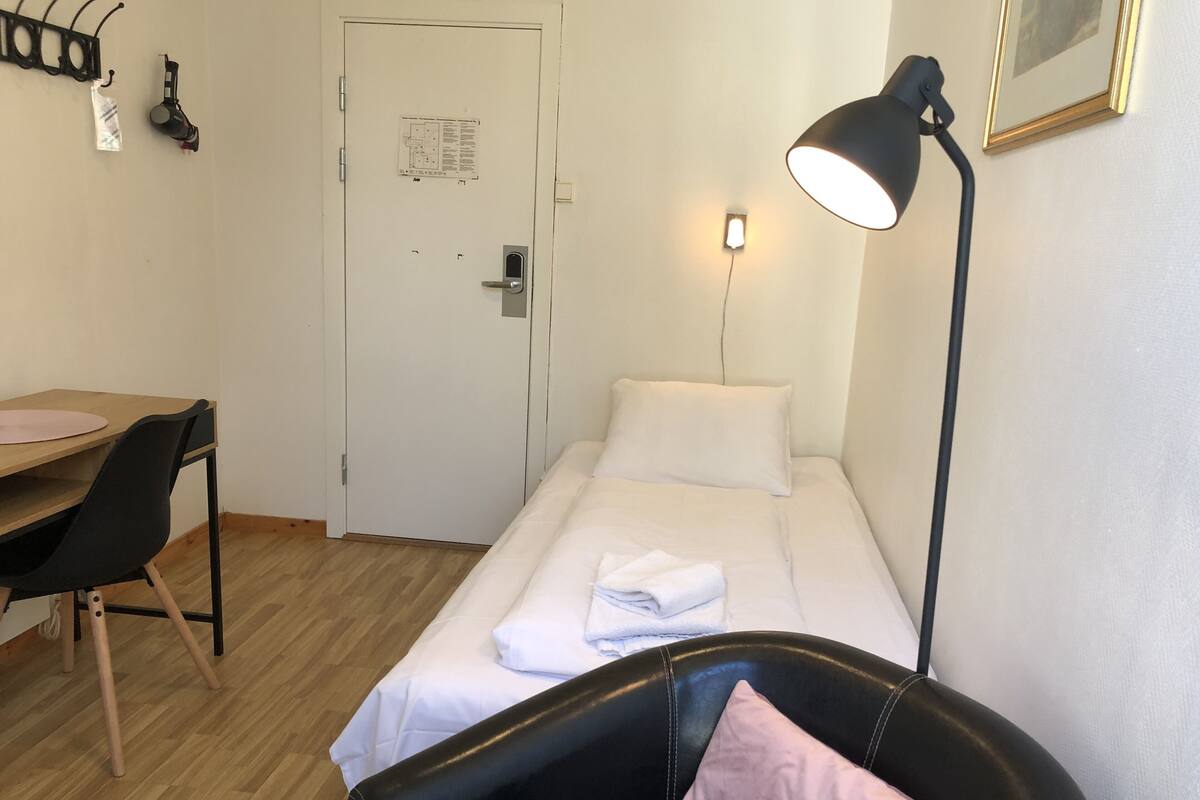 Una habitación pequeña y limpia con una cama, un escritorio, una silla y una lámpara de escritorio.