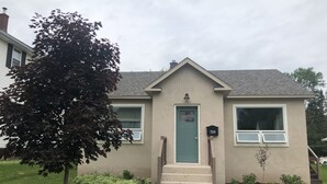 Una casa a un piano con una porta verde, il numero 709, e un piccolo giardino anteriore con un albero e degli arbusti.