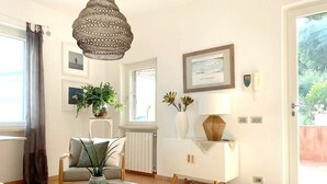 A well-lit living room with a round coffee table, a sofa, a cabinet, and a hanging light fixture. - La BouganVilla Charme & Relax with sea view (finale ligure)