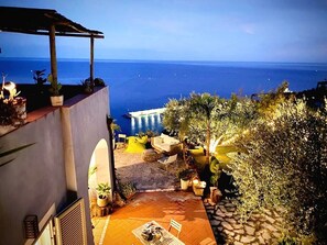 A terrace with a view of the sea, outdoor seating, and potted plants.