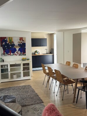 A modern kitchen with dark cabinets, a dining area with wicker chairs, and a large painting on the wall.