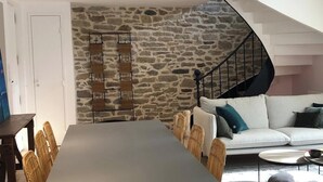 A modern living room with a stone wall, a white sofa, a dining table, and a spiral staircase.