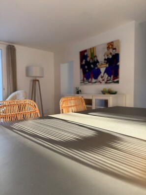 A modern room with a dining table, wicker chairs, a lamp, and a painting on the wall.